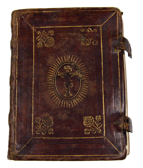 The leather cover of the Noted Hymnal. It is dark red with faded gold detailing and a depiction of Jesus on the Cross in the middle.